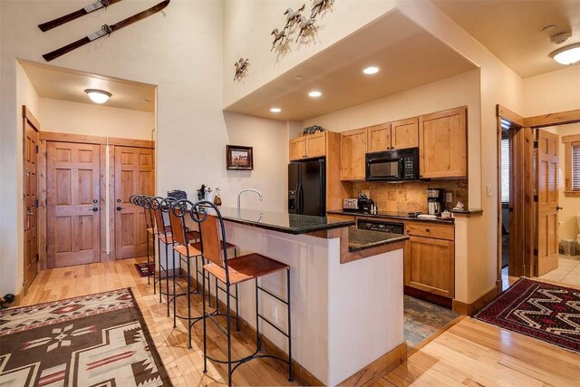 kitchen with dark stone counters, decorative backsplash, a breakfast bar, a kitchen island, and black appliances