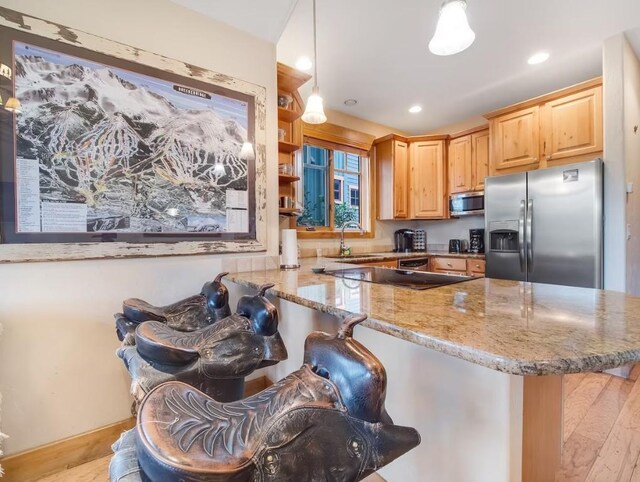 kitchen with light stone counters, kitchen peninsula, decorative light fixtures, a breakfast bar, and appliances with stainless steel finishes