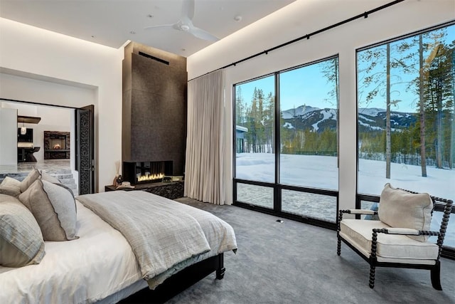 carpeted bedroom with access to exterior, a mountain view, a large fireplace, and ceiling fan