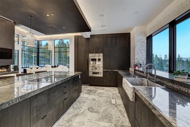 kitchen with sink, stainless steel double oven, dark stone counters, decorative light fixtures, and black electric cooktop