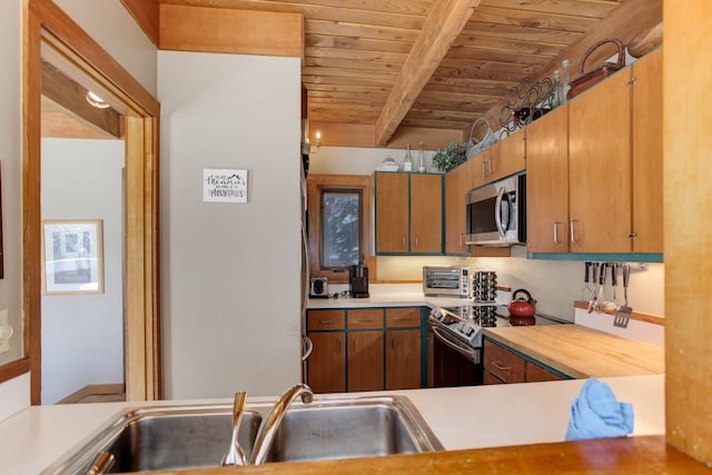 kitchen with beam ceiling, brown cabinets, stainless steel appliances, light countertops, and a sink