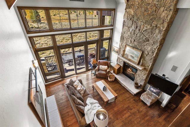 living room featuring a stone fireplace, a towering ceiling, and hardwood / wood-style flooring