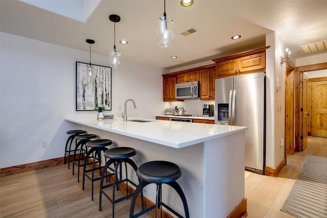 kitchen with a breakfast bar area, hanging light fixtures, light wood-type flooring, appliances with stainless steel finishes, and backsplash