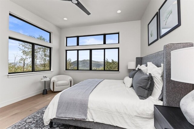 bedroom featuring a mountain view, wood-type flooring, multiple windows, and ceiling fan