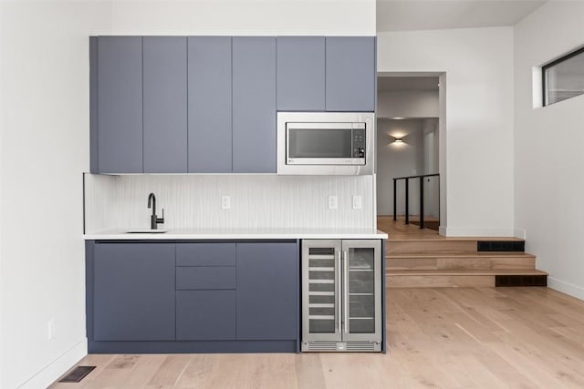 kitchen with decorative backsplash, stainless steel microwave, wine cooler, and light hardwood / wood-style flooring