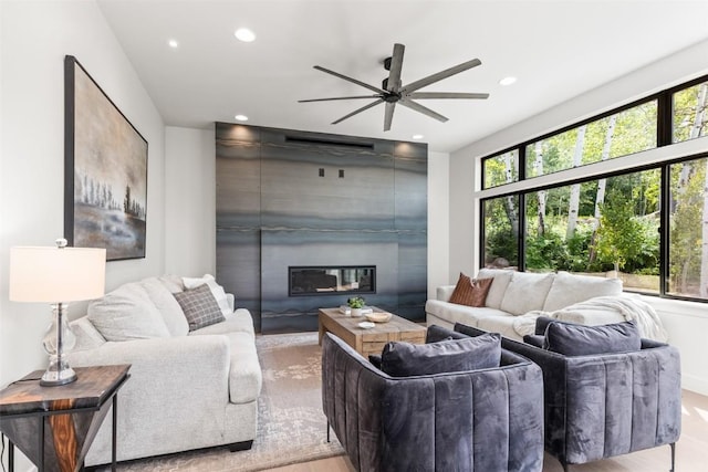 living room featuring a large fireplace, ceiling fan, plenty of natural light, and light hardwood / wood-style floors