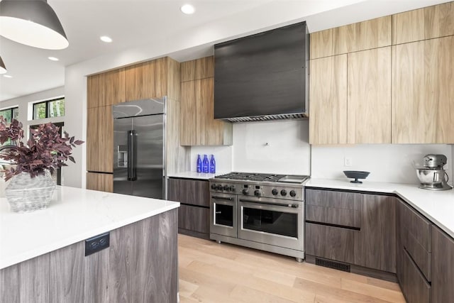 kitchen featuring high quality appliances, wall chimney exhaust hood, and light wood-type flooring