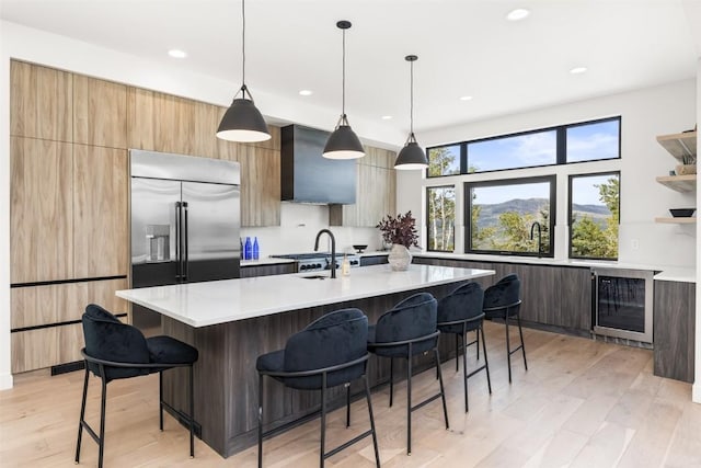 kitchen featuring an island with sink, hanging light fixtures, and wall chimney range hood