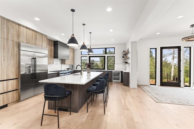 kitchen featuring premium appliances, wine cooler, hanging light fixtures, a breakfast bar area, and an island with sink