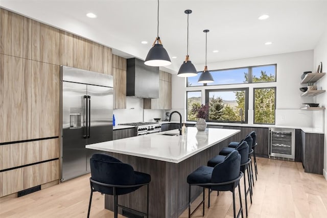 kitchen featuring a breakfast bar, premium appliances, beverage cooler, wall chimney range hood, and a center island with sink