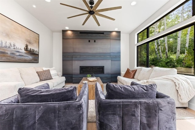 living room with ceiling fan, a large fireplace, and light wood-type flooring