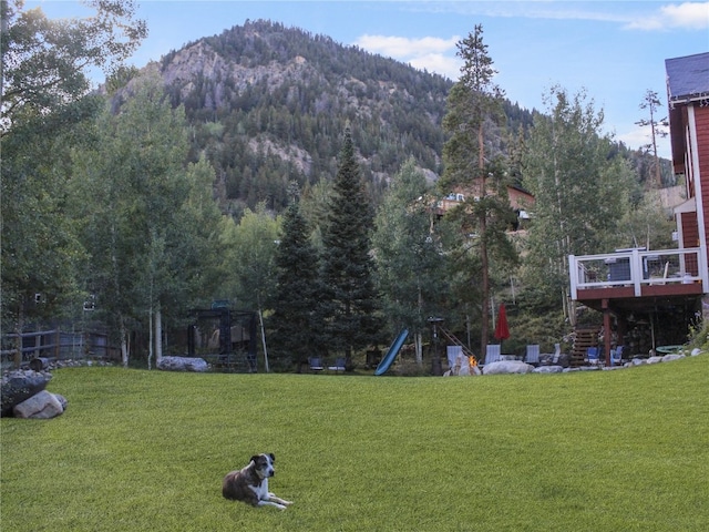 view of yard featuring a view of trees, a deck with mountain view, and a playground