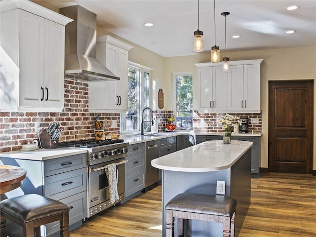 kitchen featuring wall chimney range hood, wood finished floors, premium stove, light countertops, and decorative backsplash