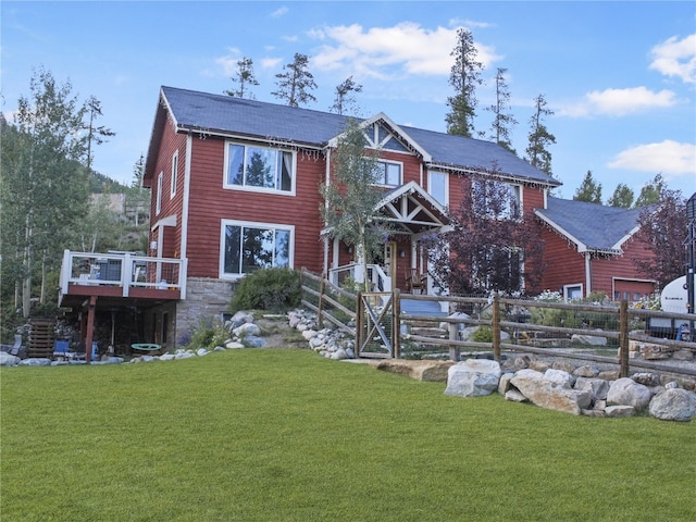 view of front facade featuring stone siding, a wooden deck, a front yard, and fence