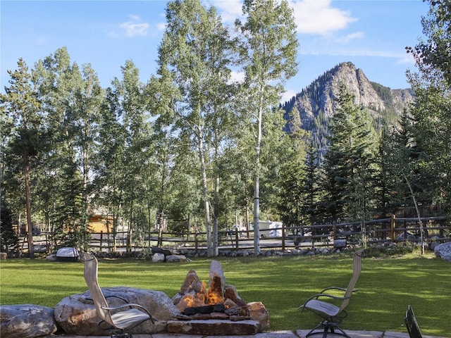 view of home's community with a mountain view, a fire pit, a lawn, and fence