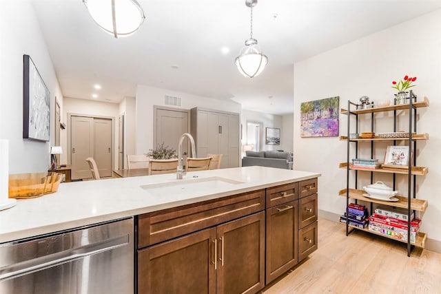 kitchen featuring decorative light fixtures, dishwasher, sink, light stone counters, and light wood-type flooring