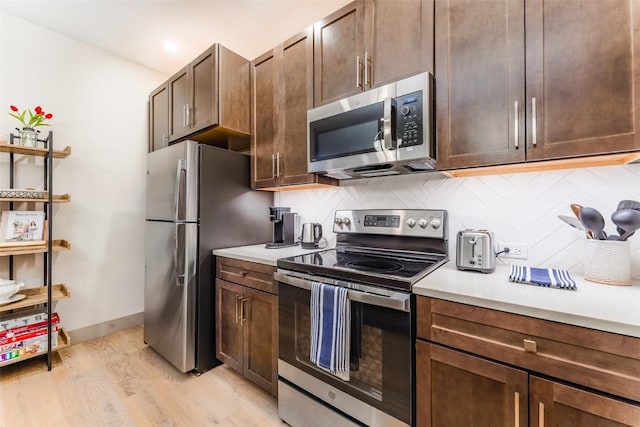 kitchen featuring appliances with stainless steel finishes, dark brown cabinets, backsplash, and light wood-type flooring