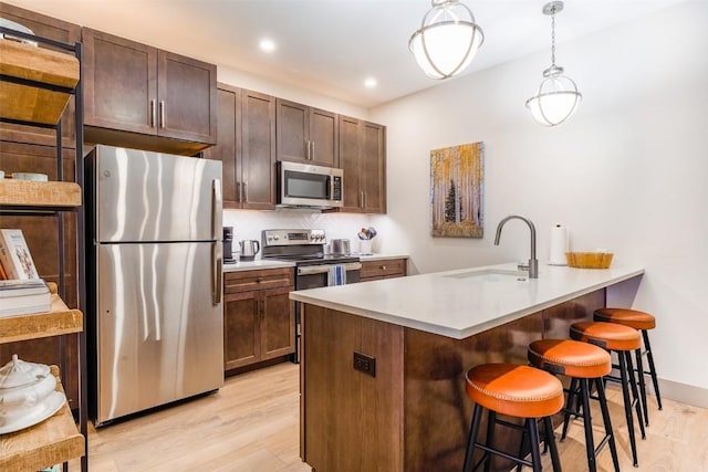 kitchen featuring pendant lighting, sink, a breakfast bar area, appliances with stainless steel finishes, and light hardwood / wood-style floors