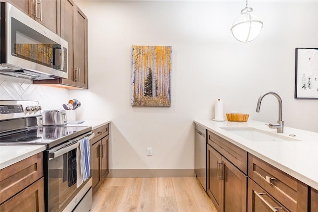 kitchen with pendant lighting, sink, stainless steel appliances, tasteful backsplash, and light wood-type flooring