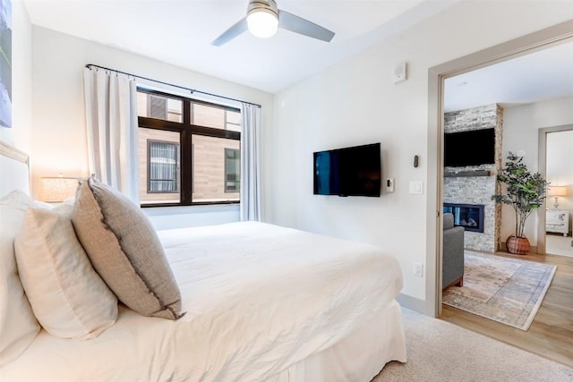 bedroom featuring ceiling fan, a stone fireplace, and light hardwood / wood-style floors