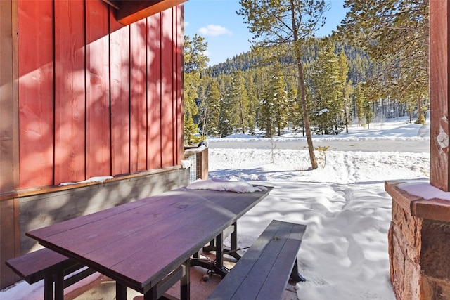 snow covered patio with a forest view and outdoor dining area