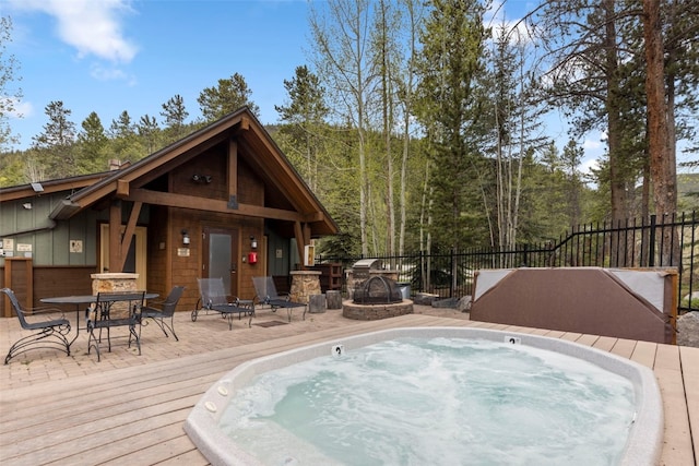 view of pool with outdoor dining area, hot tub deck surround, fence, a fire pit, and a wooden deck