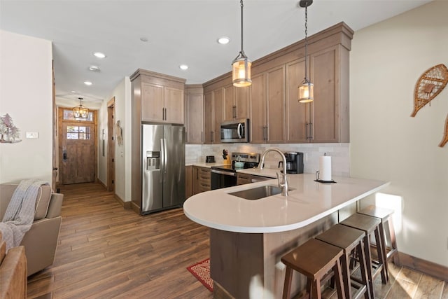 kitchen featuring a peninsula, a sink, light countertops, appliances with stainless steel finishes, and backsplash