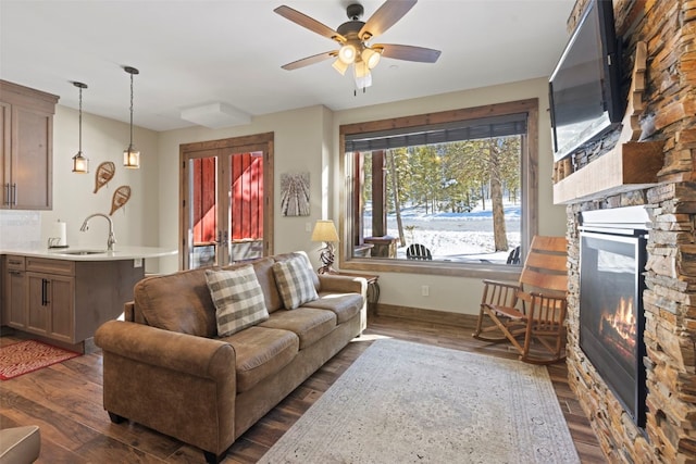 living room with ceiling fan, baseboards, dark wood-type flooring, and a stone fireplace