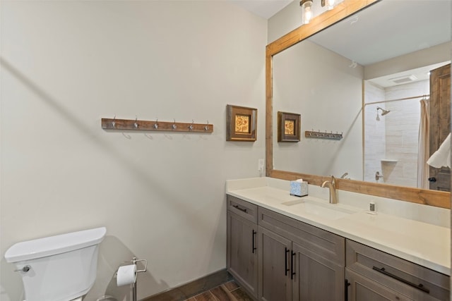 bathroom with toilet, wood finished floors, vanity, baseboards, and a shower