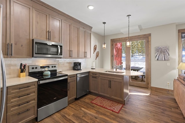 kitchen with tasteful backsplash, dark wood-style flooring, a peninsula, stainless steel appliances, and a sink