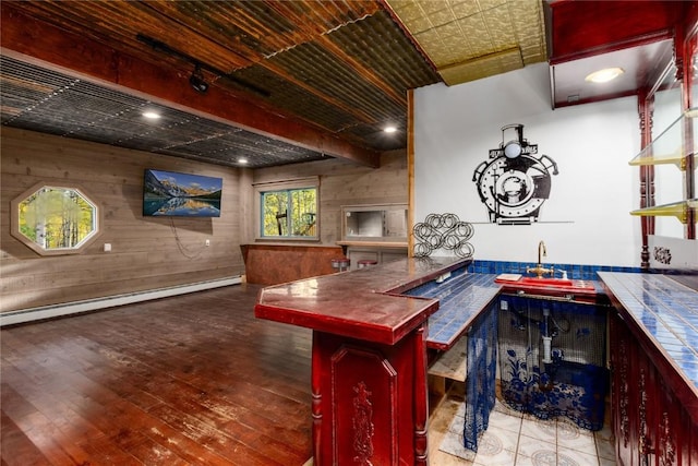 bar featuring baseboard heating, wood walls, tile counters, and hardwood / wood-style flooring