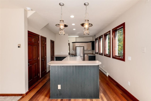 kitchen with stainless steel refrigerator, sink, a baseboard heating unit, decorative light fixtures, and a center island with sink