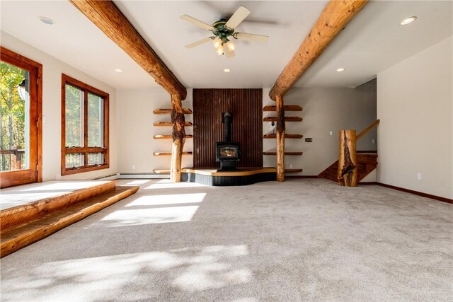 unfurnished living room with carpet flooring, a wood stove, ceiling fan, and beamed ceiling