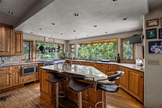 kitchen featuring light hardwood / wood-style flooring, stainless steel microwave, a breakfast bar area, and an island with sink