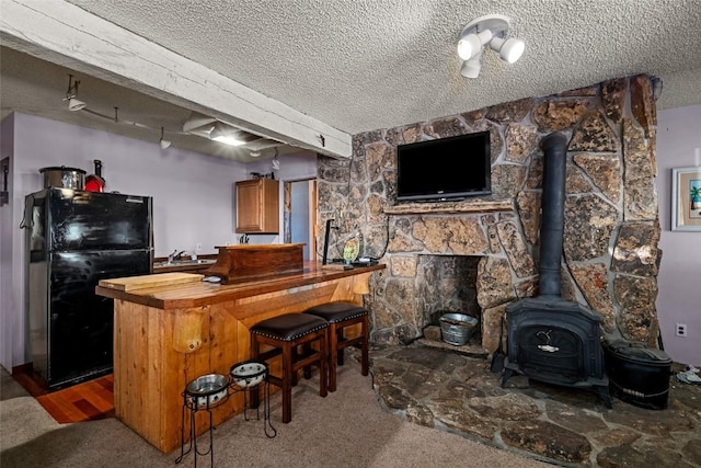 bar featuring a wood stove, black fridge, carpet, and a textured ceiling