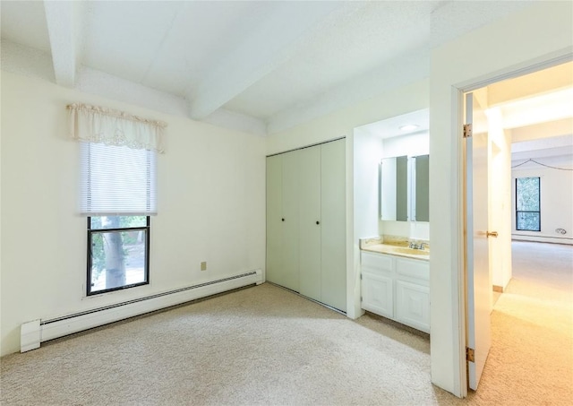 unfurnished bedroom featuring beamed ceiling, a baseboard heating unit, ensuite bathroom, light colored carpet, and a closet