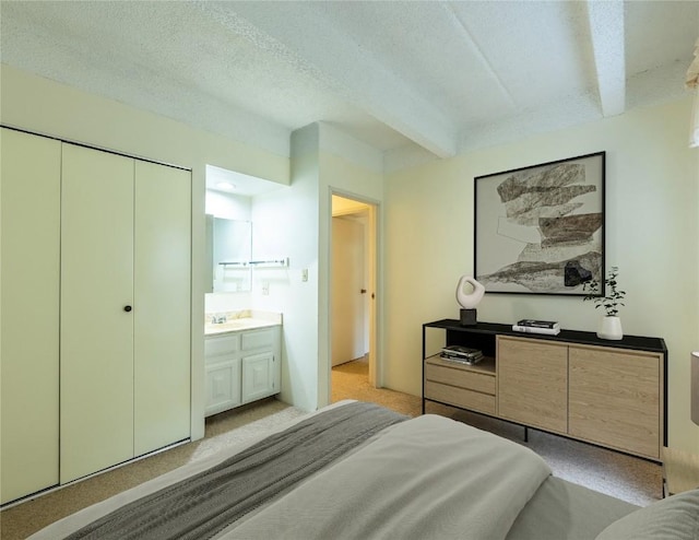 bedroom featuring connected bathroom, light carpet, beamed ceiling, and a textured ceiling