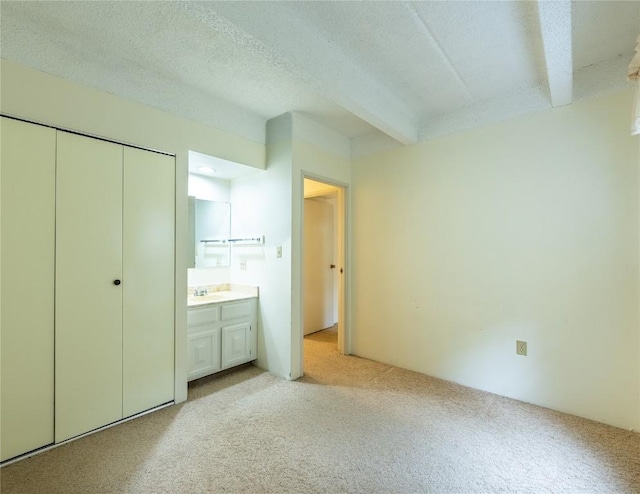 unfurnished bedroom with light carpet, sink, beamed ceiling, connected bathroom, and a closet