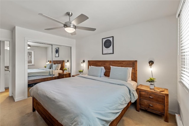 bedroom featuring a baseboard heating unit, light colored carpet, a closet, and ceiling fan