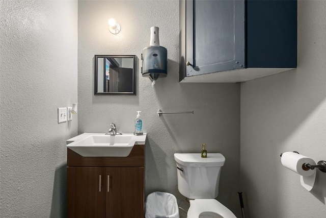 half bath with toilet, a textured wall, and vanity