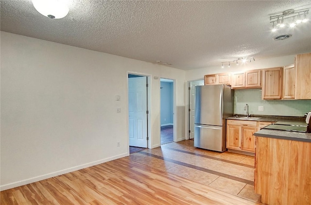 kitchen featuring light brown cabinets, sink, stainless steel fridge, stove, and a textured ceiling