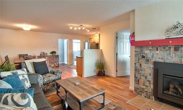 living room featuring a tiled fireplace, a textured ceiling, light wood-type flooring, and baseboards