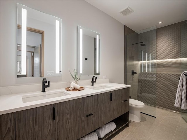 bathroom with tile patterned flooring, vanity, toilet, and a tile shower