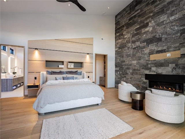 bedroom featuring ceiling fan, a stone fireplace, light wood-type flooring, and a towering ceiling