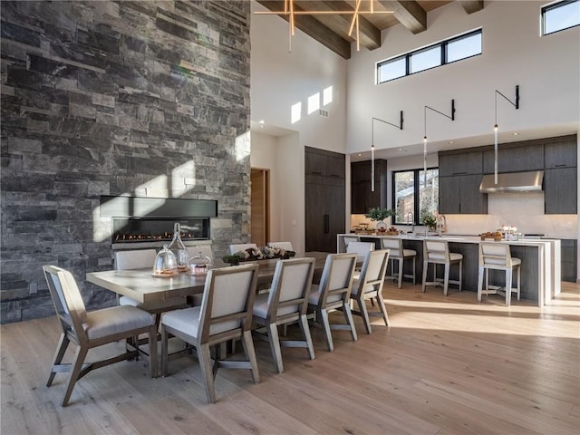 dining space featuring beamed ceiling, a towering ceiling, and light hardwood / wood-style floors