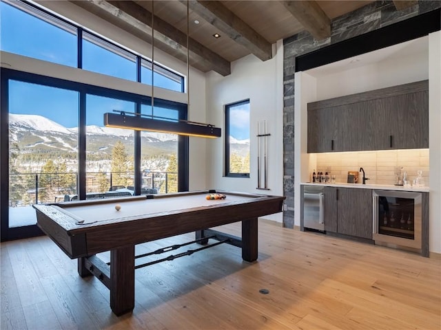 recreation room with a mountain view, wine cooler, billiards, light hardwood / wood-style flooring, and beamed ceiling