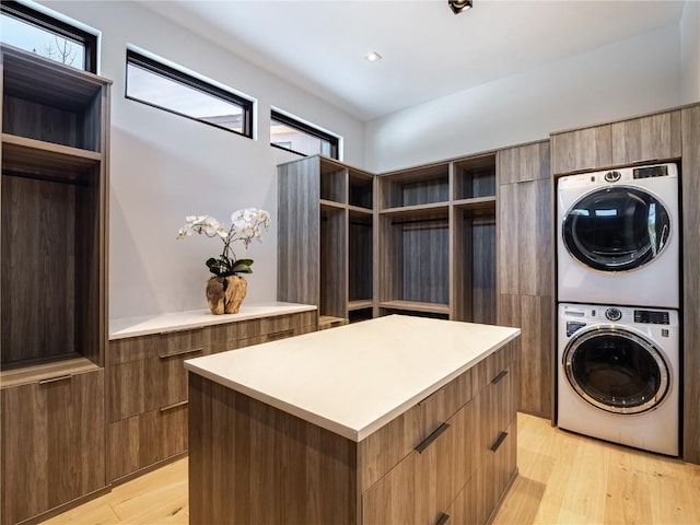 laundry area with stacked washer / dryer, cabinets, and light wood-type flooring