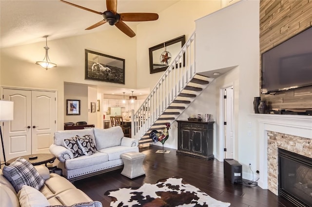 living room featuring a textured ceiling, ceiling fan, dark wood-type flooring, high vaulted ceiling, and a stone fireplace