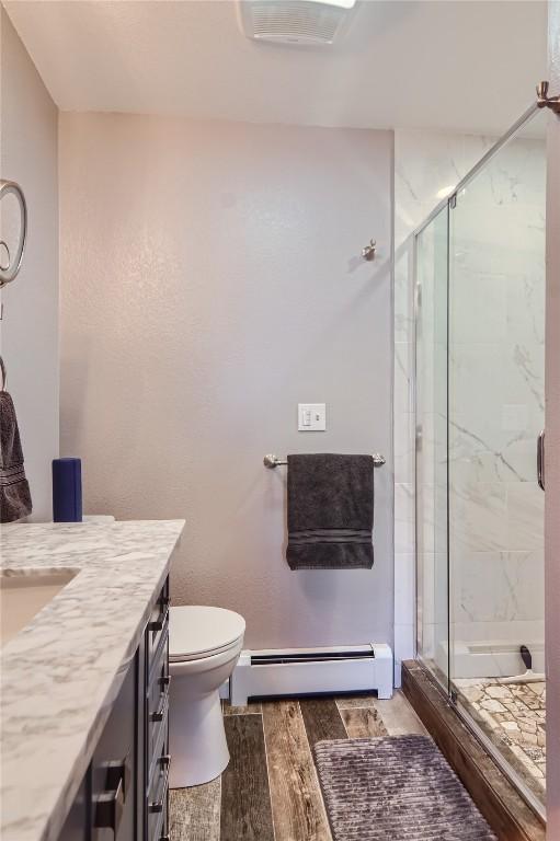 bathroom with vanity, toilet, an enclosed shower, and baseboard heating