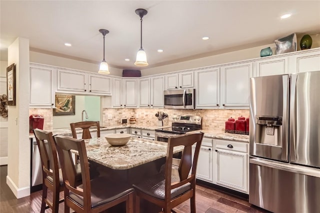 kitchen featuring white cabinets, hanging light fixtures, light stone counters, appliances with stainless steel finishes, and dark hardwood / wood-style flooring